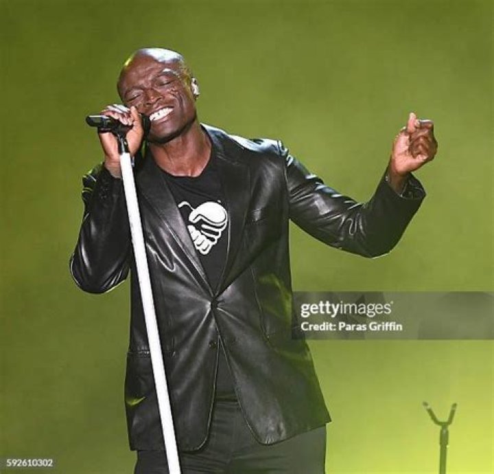 Seal performing on a stage with a guitar and singing into a microphone